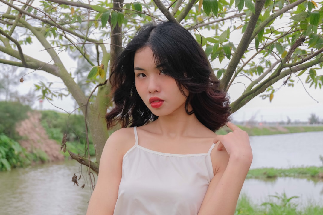 a woman standing next to a tree near a body of water